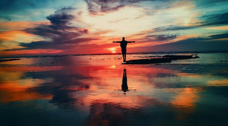 silhouette of person standing on rock surrounded by body of water